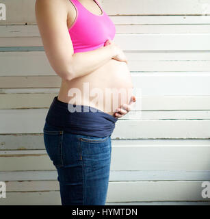 Close up ritratto di una giovane donna incinta holding stomaco - Vista laterale Foto Stock