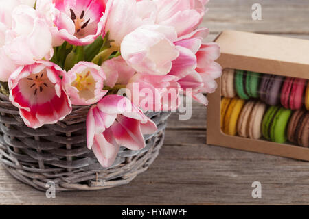 Rosa bouquet di tulipani cesto e amaretti sul tavolo di legno Foto Stock