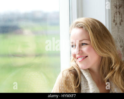 Close up ritratto di una donna sorridente guardando al di fuori attraverso la finestra Foto Stock