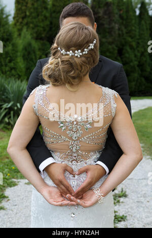 Lo sposo facendo un segno di cuore con le sue mani tenendo braccia intorno alla sua sposa Foto Stock