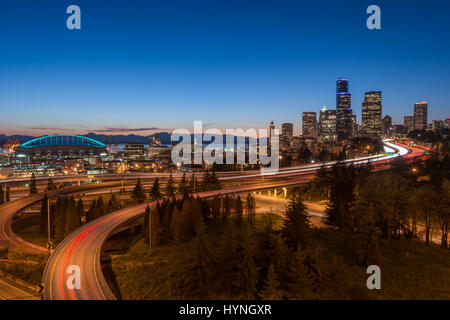 Seattle Skyline al crepuscolo con la superstrada che si avvicina alla città con Interstate 90 e 5 piena di treni leggeri traffico in movimento in arrivo e in arrivo Foto Stock