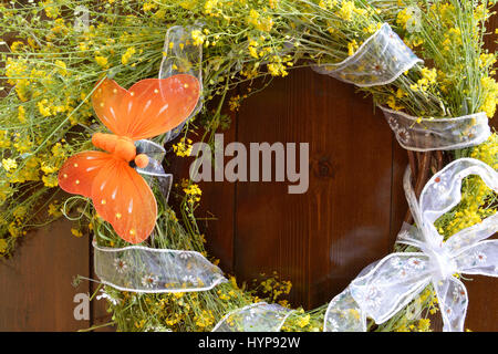 Ghirlanda di giallo fiori selvatici e decorate con una farfalla arancione su sfondo di legno Foto Stock