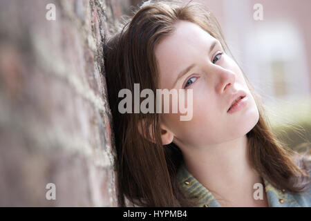 Close up ritratto di un simpatico giovane donna appoggiata contro un muro di mattoni all'aperto Foto Stock