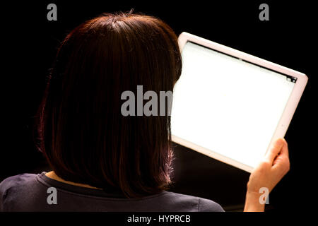 Donna che guarda l'iPad Pro tenuto in mano contro lo sfondo nero Foto Stock