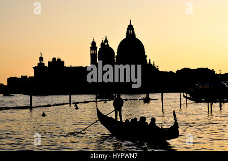Silhouette di Santa Maria della Salute a Venezia al tramonto con una gondola in movimento lungo il canale. Foto Stock