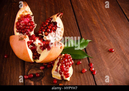 Succosa melograno su assi di legno.tagliate in pezzi di ripe melograno. la melagrana è maturo. maturi i semi di melograno. fresche foglie succosa Foto Stock