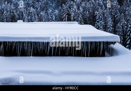 Ghiaccioli formata appesi da grondaia della coperta di neve chalet di montagna Foto Stock