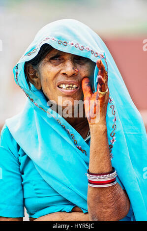 Jodhpur, India, settembre 10, 2010: vecchia donna indiana in blu saree che mostra i suoi denti cercando ona un fotografo di henna sulla sua mano e braccialetti Foto Stock