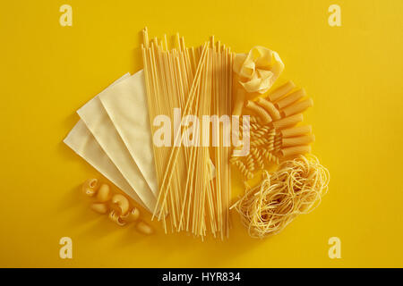 Un assortimento di tipi di pasta su sfondo giallo. Varie forme di pasta, spaghetti, lasagne, fusilli e altri. Foto Stock