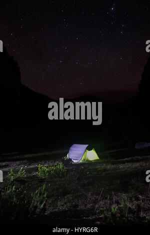 Paesaggio notturno con lone, popolato e illuminato di facile passo (pop-up) tenda in piedi su un alpeggio sotto il cielo stellato. Uno stile di vita all'aperto e sl Foto Stock