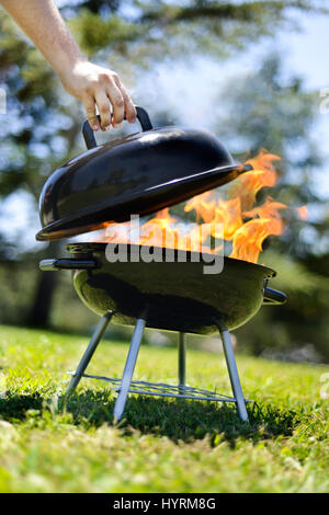 Fire fuoriesce dalla griglia mentre il coperchio viene sollevato. Grigliare gli hamburger per un picnic in California. Foto Stock