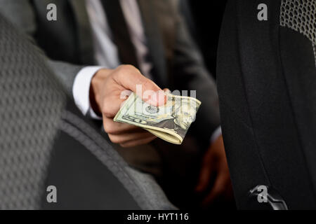 Un giovane uomo caucasico in un elegante abito grigio seduto nel sedile posteriore di una vettura offre un batuffolo di fatture del dollaro nella parte anteriore Foto Stock