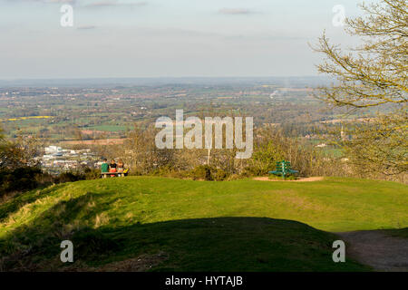 Tre giovani seduti proprio un banco su Malvern Hills guardando fuori verso Malvern Foto Stock