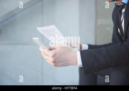 Uomo molto impegnato con lo smartphone e alcuni documenti Foto Stock