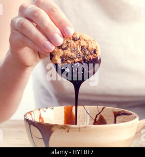 Womans mano cookie per immersione nel cioccolato fuso. Foto Stock