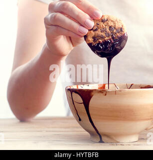 Womans mano cookie di immersione in un cioccolato fondente fuso. Messa a fuoco selettiva Foto Stock