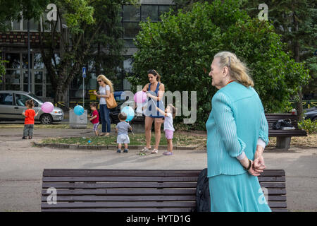 Belgrado, Serbia - Agosto 2, 2015: vecchia donna guardando le donne più giovani di prendersi cura di bambini che giocano con palloncini nel quartiere di Zemun P Foto Stock