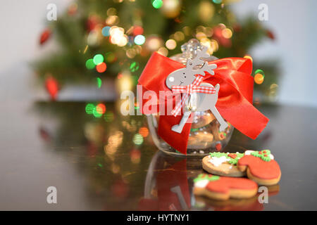 Vaso decorato con biscotti di Natale. Illuminato albero di Natale sullo sfondo Foto Stock