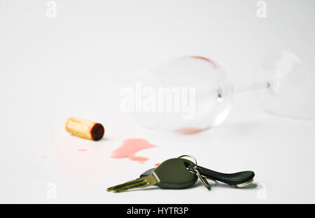 Carkeys giacente sulla superficie bianca. Caduto wineglass con fuoriuscite di vino rosso e il sughero in background.concetto non per guida in stato di ebbrezza Foto Stock