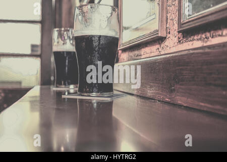 Due bicchieri della famosa nera Irish Stout nel pub irlandese sulla barra di legno Foto Stock