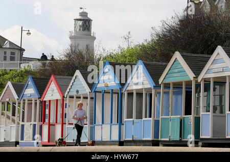Una donna cammina cani passato beach capanne lungo il fronte mare a Southwold, Suffolk, come vacanze di Pasqua le temperature di molla per altezze di summertime questo fine settimana con il giorno più caldo dell'anno dovrebbe arrivare sulle coste inglesi. Foto Stock