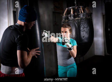 Giovane femmina boxer sportivo nella boxe Guantoni boxe training con il suo lettino e Boxing sacco da boxe in una palestra Foto Stock