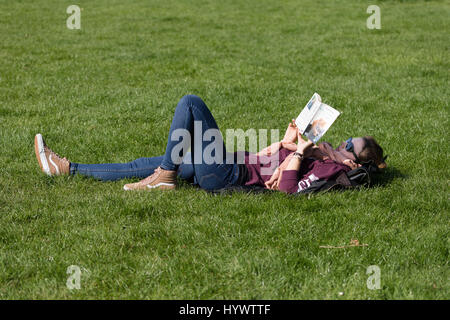 Woolwich, Londra, Regno Unito. Il 6 aprile 2017. Una donna che legge un libro in un parco vicino al Fiume Tamigi durante le giornate di sole. Quando la temperatura aumenta a Londra, fumoso smog e inquinamento avvertenze sono rilasciati a parti della capitale. Credito: Vickie Flores/Alamy Live News Foto Stock