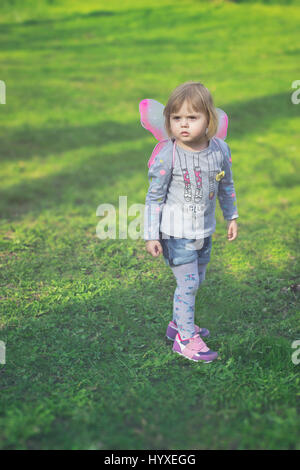 Pretty toddler ragazza con ali di farfalla, giocando nel parco Foto Stock