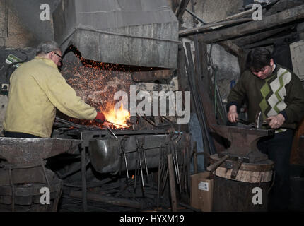 Il fabbro con un martello lavorando su un ferro da stiro riscaldato in officina Foto Stock