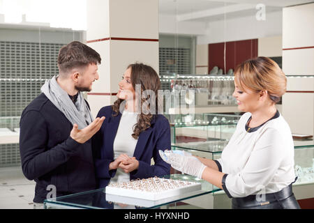 Lo abbiamo trovato sorridenti giovane guardando gli uni gli altri come il gioielliere femmina mostrando loro gli anelli di fidanzamento Foto Stock