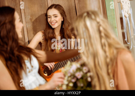 Giovane donna sorridente a suonare la chitarra e guardando i suoi amici di sesso femminile Foto Stock