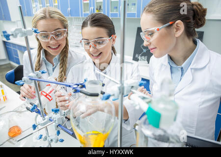 Donna sorridente scienziati degli occhiali di protezione rendendo esperimento in laboratorio chimico Foto Stock