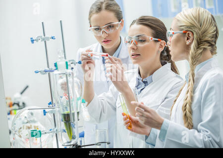Tre giovani concentrati scienziate rendendo esperimento in laboratorio chimico Foto Stock