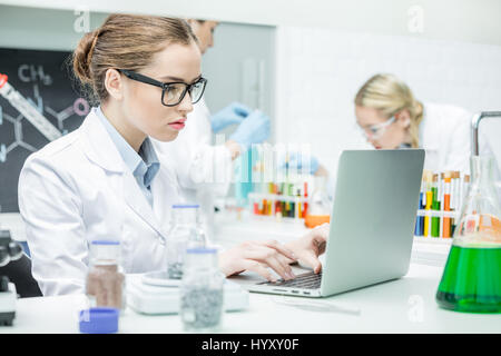 Femmina concentrato scienziato che lavora sul computer portatile in laboratorio chimico Foto Stock
