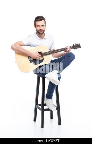 Bel giovane con la chitarra seduto su sgabello da bar isolato su bianco Foto Stock