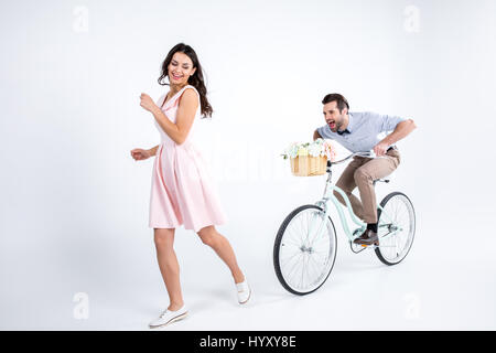 Felice giovane donna in esecuzione da uomo tanga di equitazione Bicicletta con cesto fiorito Foto Stock