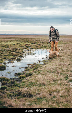 Escursionista e cane da lo stagno in prati in un giorno nuvoloso Foto Stock