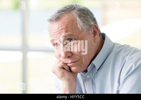 Senior con man mano sul mento che guarda lontano. Foto Stock