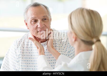 Medico donna toccando uomo senior il collo. Foto Stock