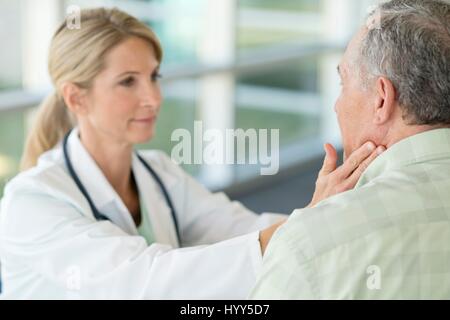 Medico donna toccando uomo senior il collo. Foto Stock