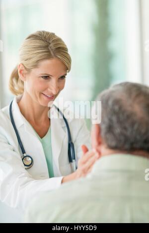 Medico donna toccando uomo senior il collo. Foto Stock