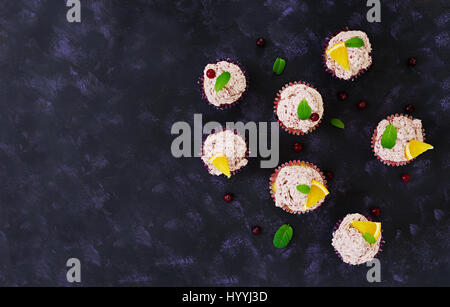 Tortini al limone con crema di ciliegia. Mirtillo rosso, foglie di menta. Cibo su uno sfondo scuro. Vista superiore Foto Stock