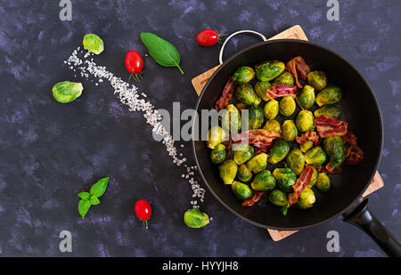 Arrosto di cavolini di Bruxelles con pancetta affumicata su sfondo scuro. Vista superiore Foto Stock