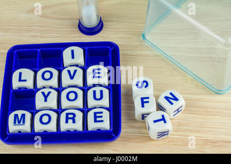 Ti amo più formulazione blocchi del gioco in blu il vassoio su una superficie di legno con timer di sabbia e il coperchio del vassoio di alimentazione sul retro Foto Stock