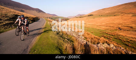 Due ciclisti salire uno stretto vicolo del paese attraverso la montagna paesaggio di brughiera del Newlands Valley vicino a Keswick in Inghilterra del Lake District. Foto Stock