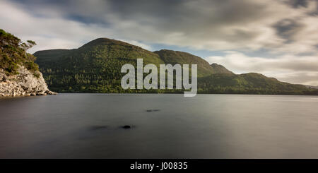 Serata sole splende sulle sponde rocciose di Muckross Lake e le boscose pendici del monte Torc in Irlanda il Parco Nazionale di Killarney. Foto Stock