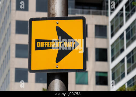 Direzionale segno giallo con messaggio concettuale diverso modo sulla freccia nera su defocalizzata ufficio edificio dello sfondo. Foto Stock