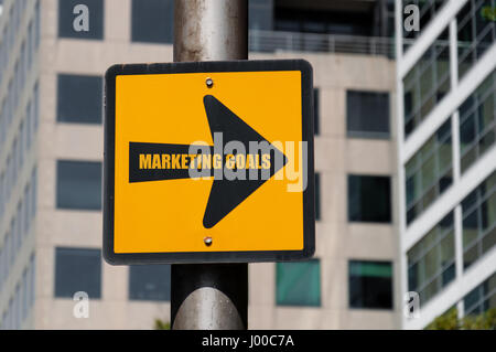 Direzionale segno giallo con messaggio concettuale obiettivi di marketing sulla freccia nera su defocalizzata ufficio edificio dello sfondo. Foto Stock