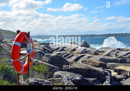 Lifesavers anello su piattaforme rocciose sulla costa rocciosa con le onde che si infrangono e Sydney skyline della città in background, Nuovo Galles del Sud, Australia. Foto Stock