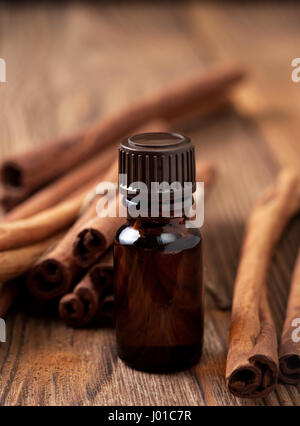 Bottiglia di vetro con olio essenziale di cannella, bastoncini di cannella su uno sfondo di legno Foto Stock